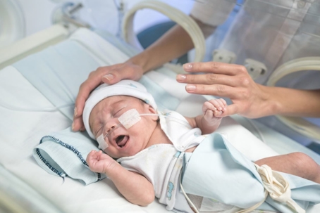 Baby in incubator yawning while parents hands come through holes