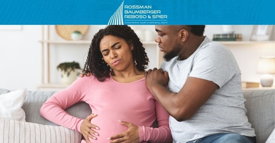 pregnant woman uncomfortable holding stomach while partner comforts her